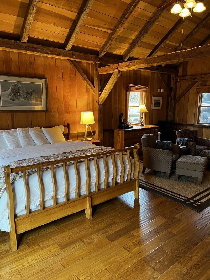 A warm, rustic cabin with a wooden vaulted ceiling, exposed beams, a king bed, and a comfortable seating area, all on hardwood floors.