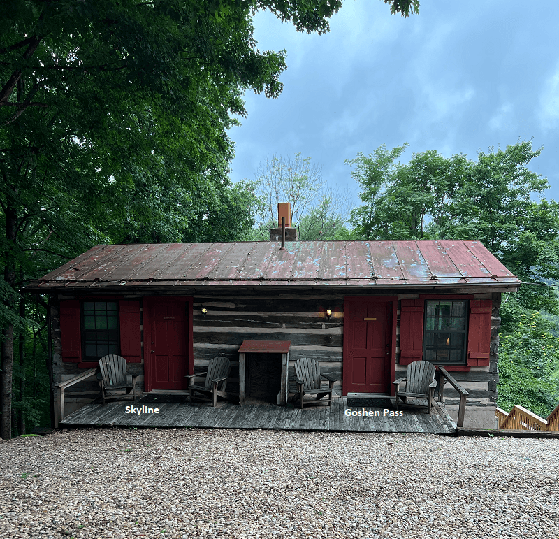 A charming rustic cabin featuring red doors, red window shutters, and a front porch with chairs.