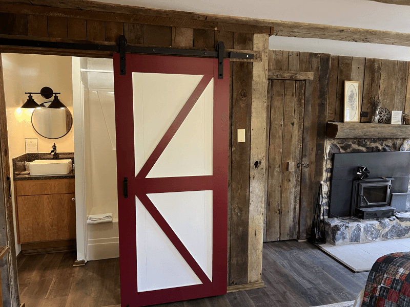Classic barn door leading to private bathroom. Also shown is an inviting wood burning fireplace set in a stone surround.