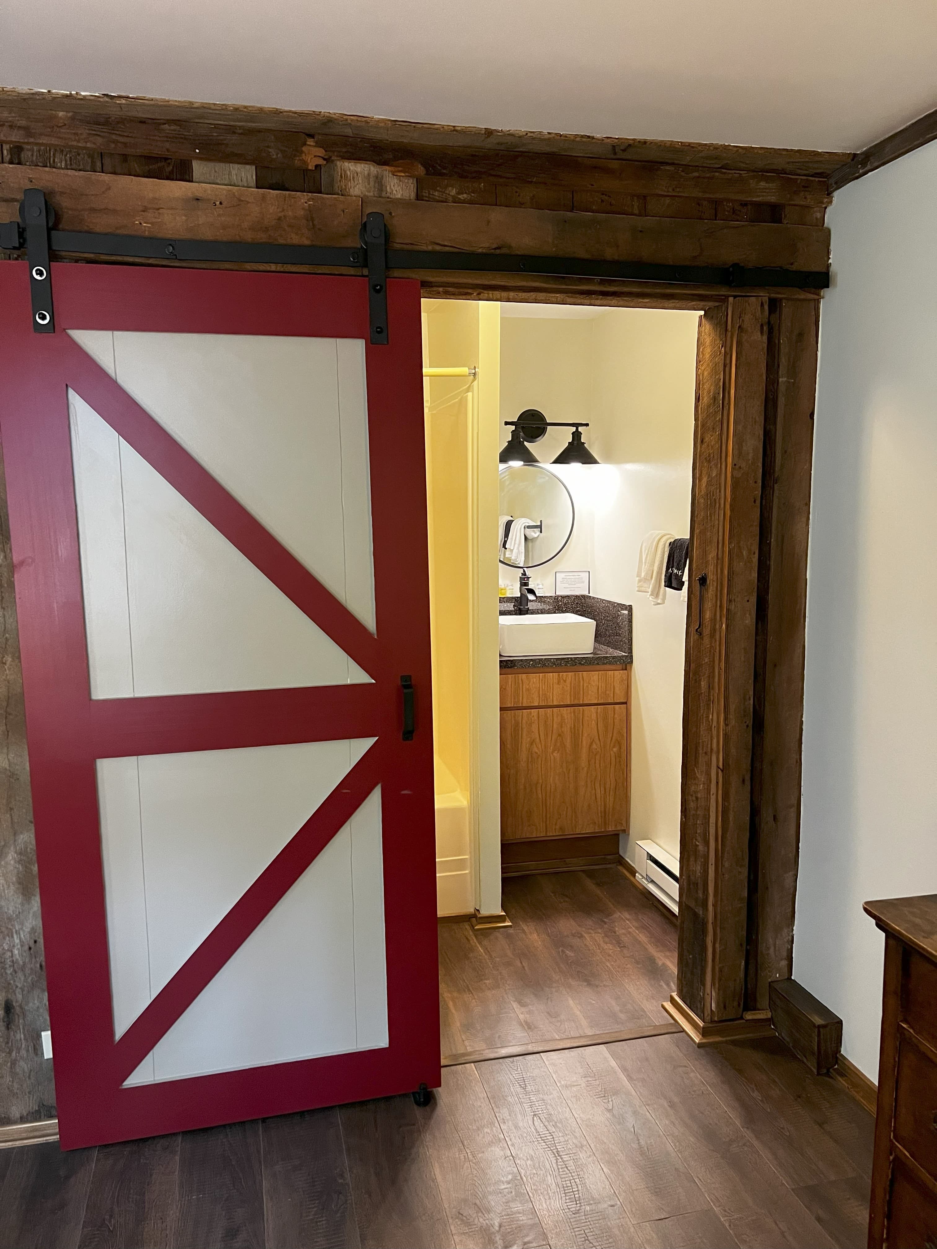 Red and white barn door opens to a bathroom with a vessel sink and round mirror.