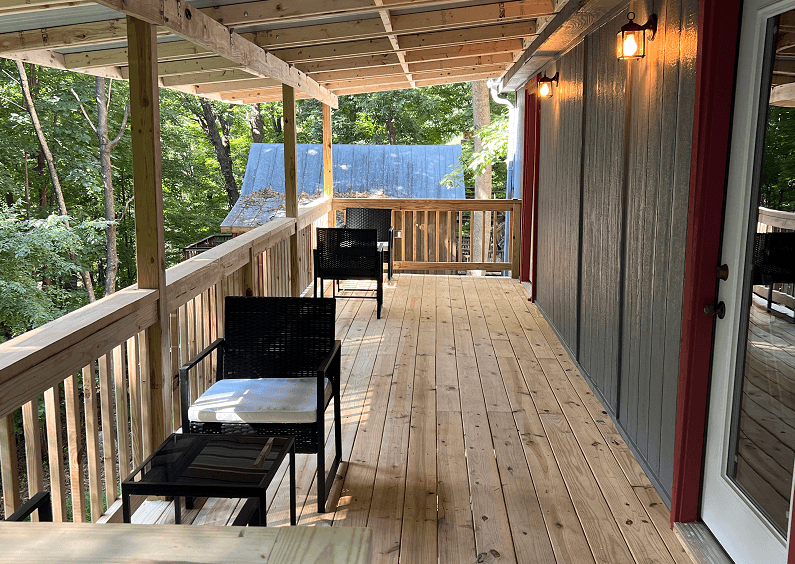 A spacious outdoor wooden deck with several black chairs and small tables, overlooking a wooded area.