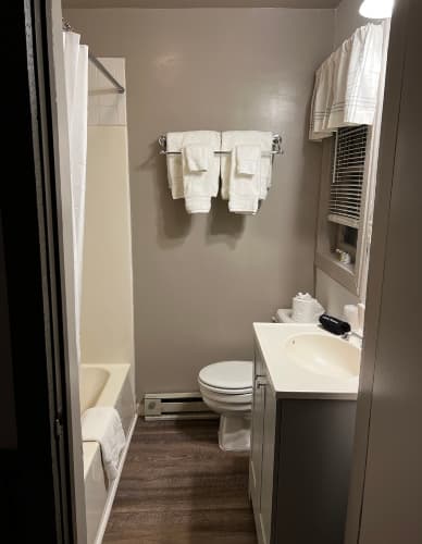 A compact bathroom with a bathtub and shower, a toilet, a vanity with a sink, and several white towels hanging on wall racks.