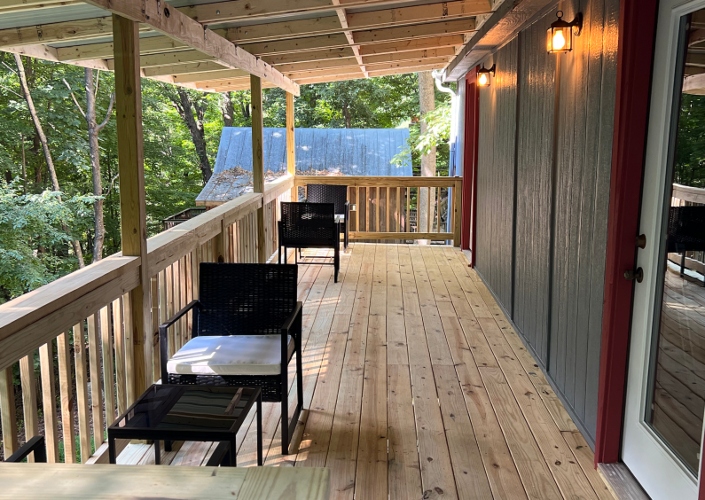 A spacious outdoor wooden deck with several black chairs and small tables, overlooking a wooded area.