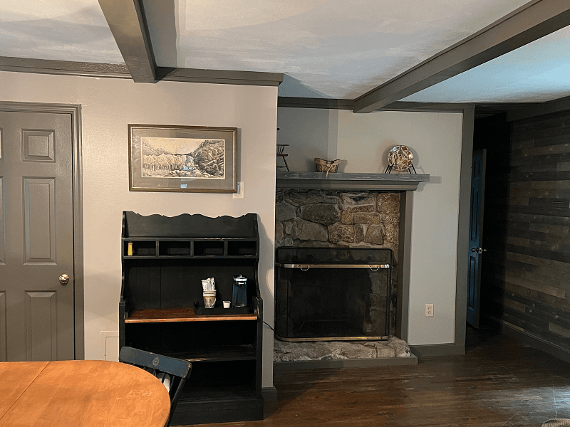 A cozy room with a stone fireplace, a dark hutch, and a wooden table partially visible in the foreground.