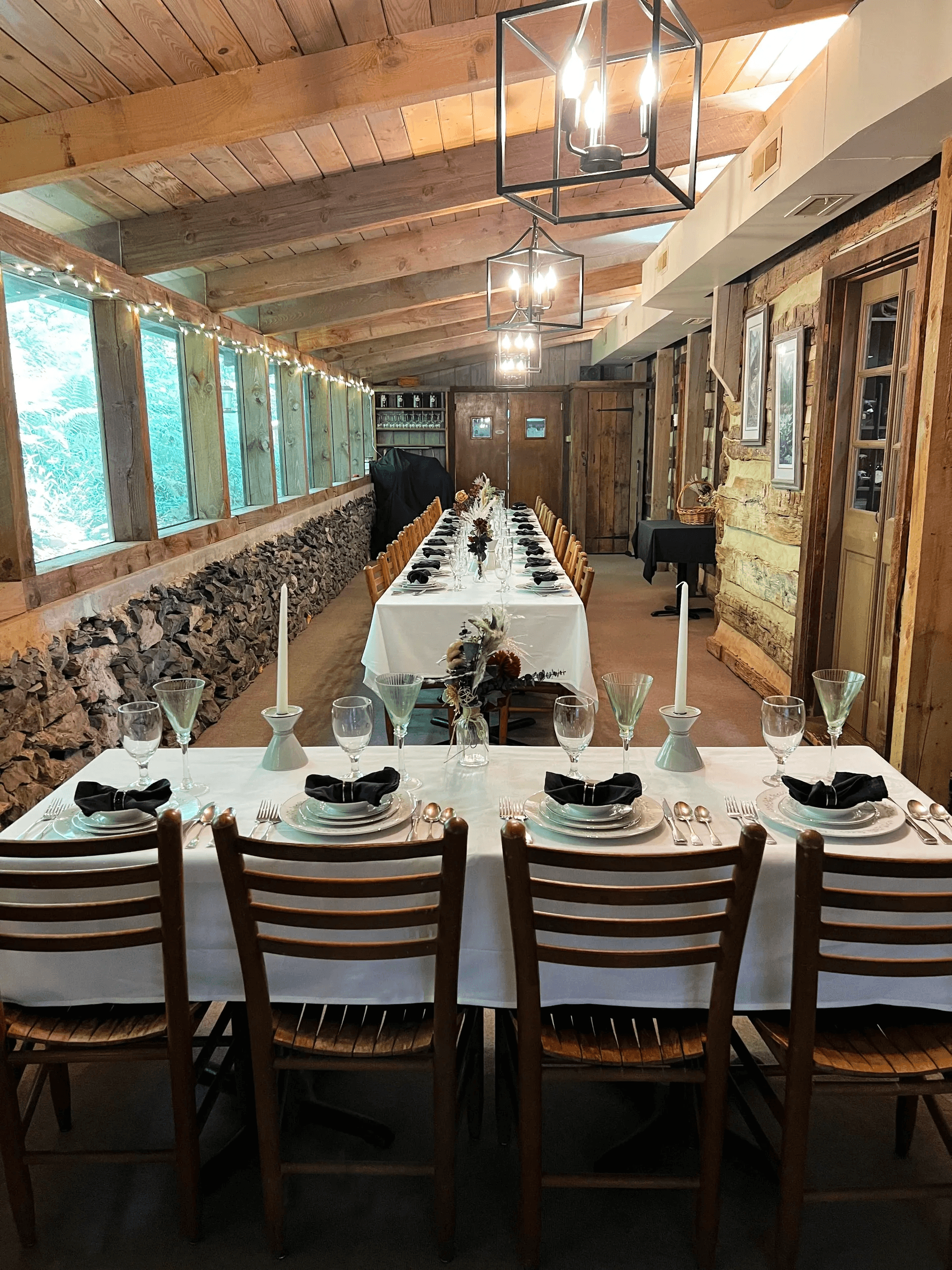 A beautifully set long dining table in a rustic space with wooden walls and elegant lighting.