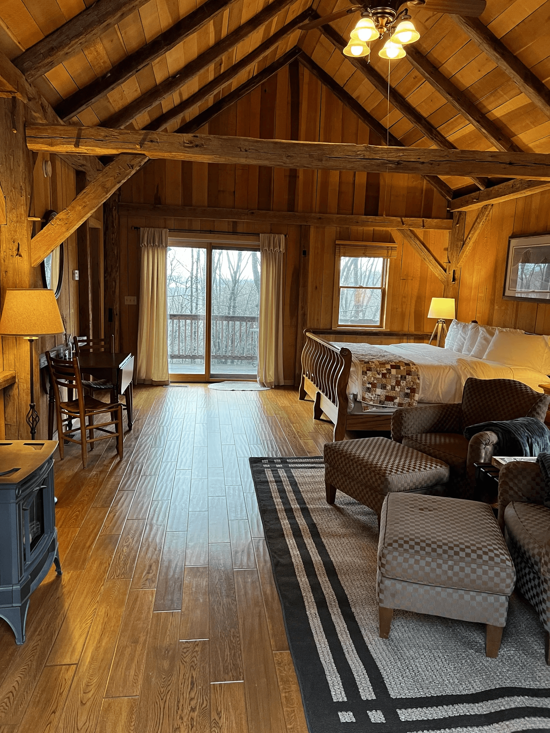 A cozy, wooden cabin interior featuring a king-sized bed, seating area, and large windows with a view.