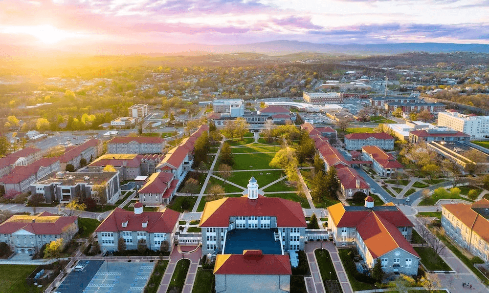 Aerial view of a university campus at sunset, featuring red-roofed buildings and green spaces.
