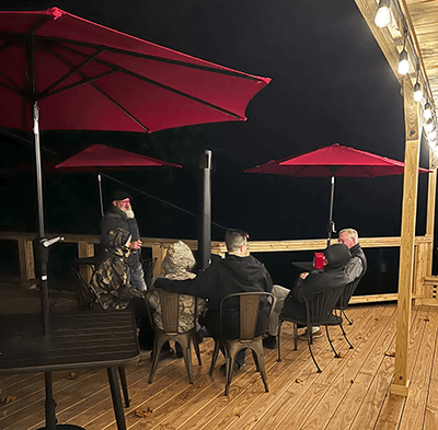 A group of five people seated under red umbrellas on a wooden deck at night.
