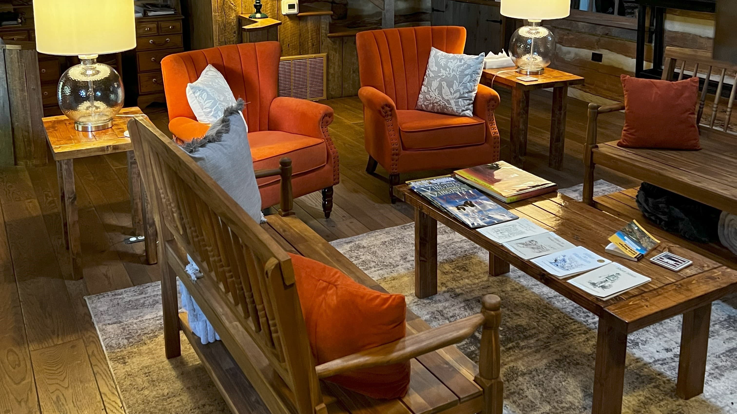 Cozy living room featuring orange armchairs, a wooden bench, and a coffee table with books, set in a warm, rustic ambiance.