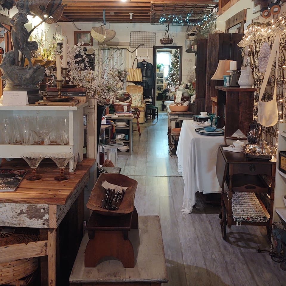 A cozy vintage shop filled with eclectic furnishings and decor, leading to a warmly lit back area.