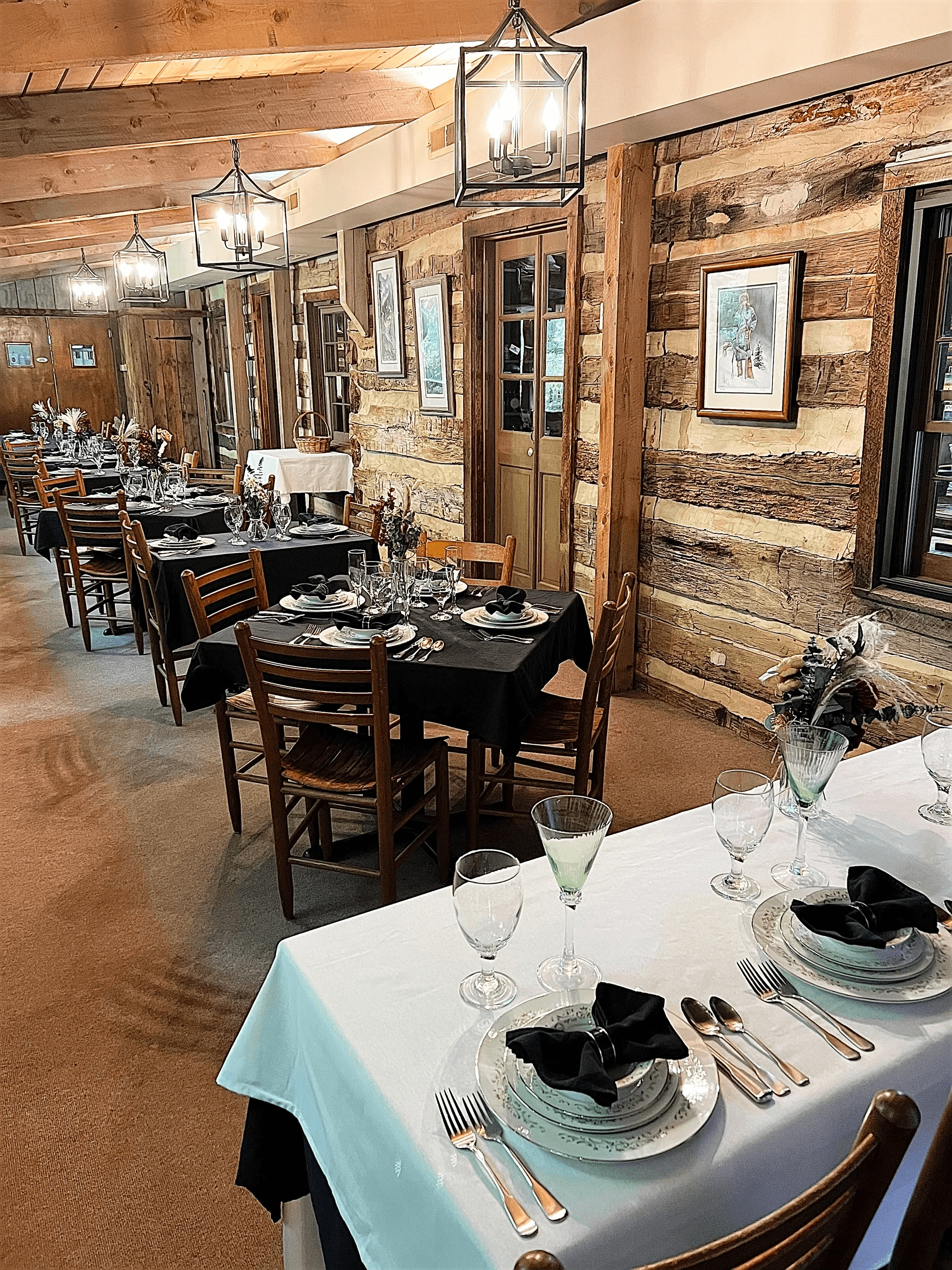 A cozy dining room featuring elegantly set tables, rustic wooden walls, and warm lighting.
