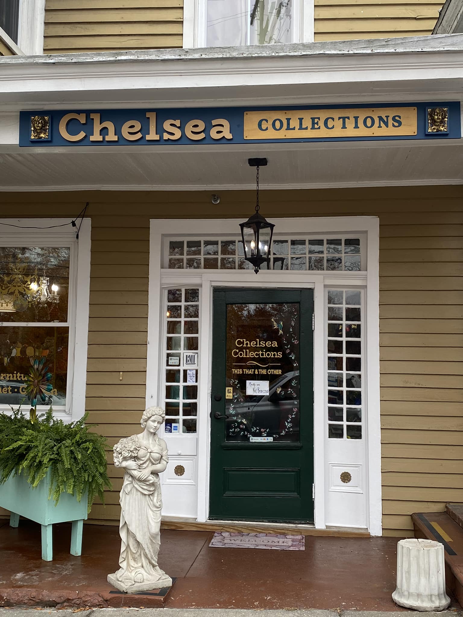Front entrance of Chelsea Collections shop featuring a green door, decorative hanging lantern, and a statue.