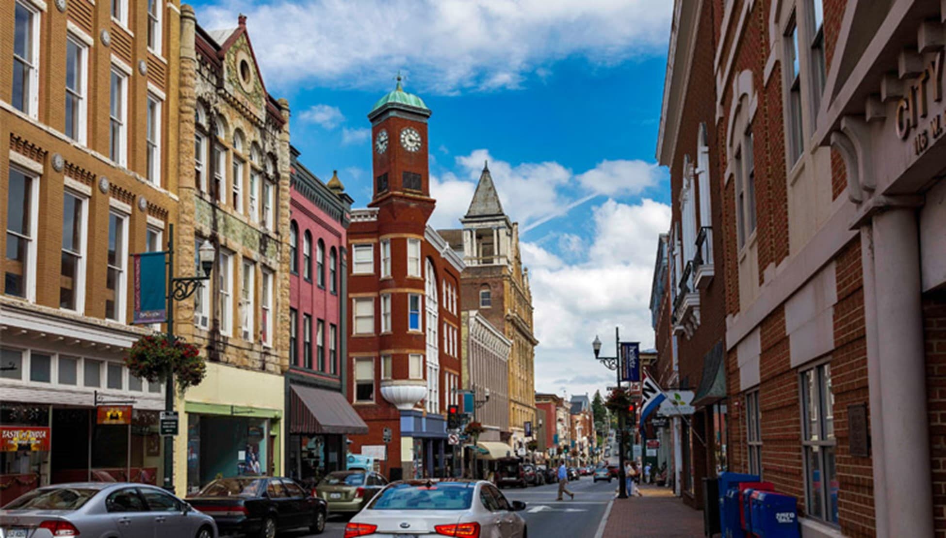 A scenic view of a historic downtown street featuring brick buildings and a clock tower under a blue sky.