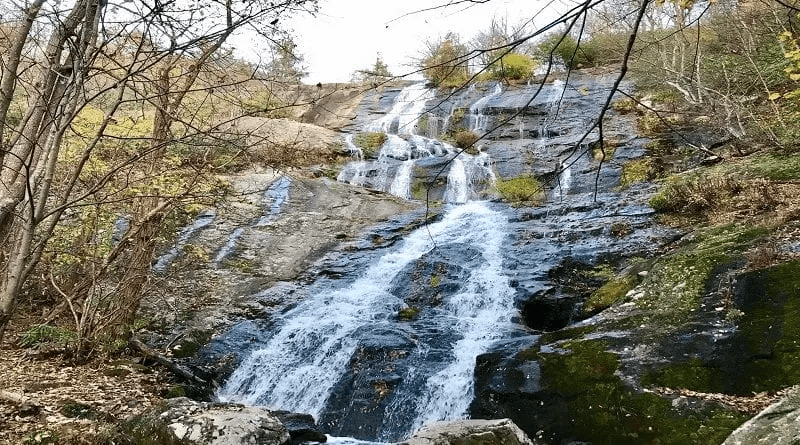 A cascading waterfall flows down rocky terrain, surrounded by autumn foliage. A cascading waterfall flows down rocky terrain, surrounded by autumn foliage.