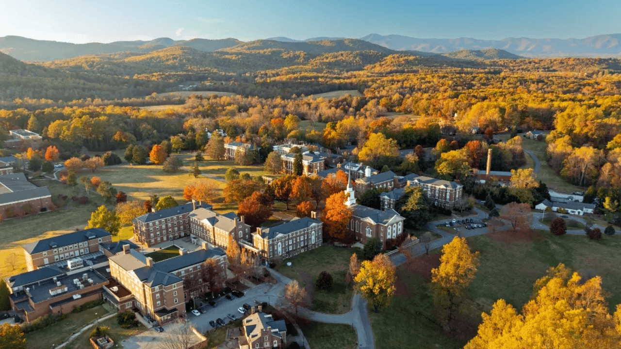 Aerial view of a collegiate campus surrounded by colorful autumn foliage and mountains in the background.