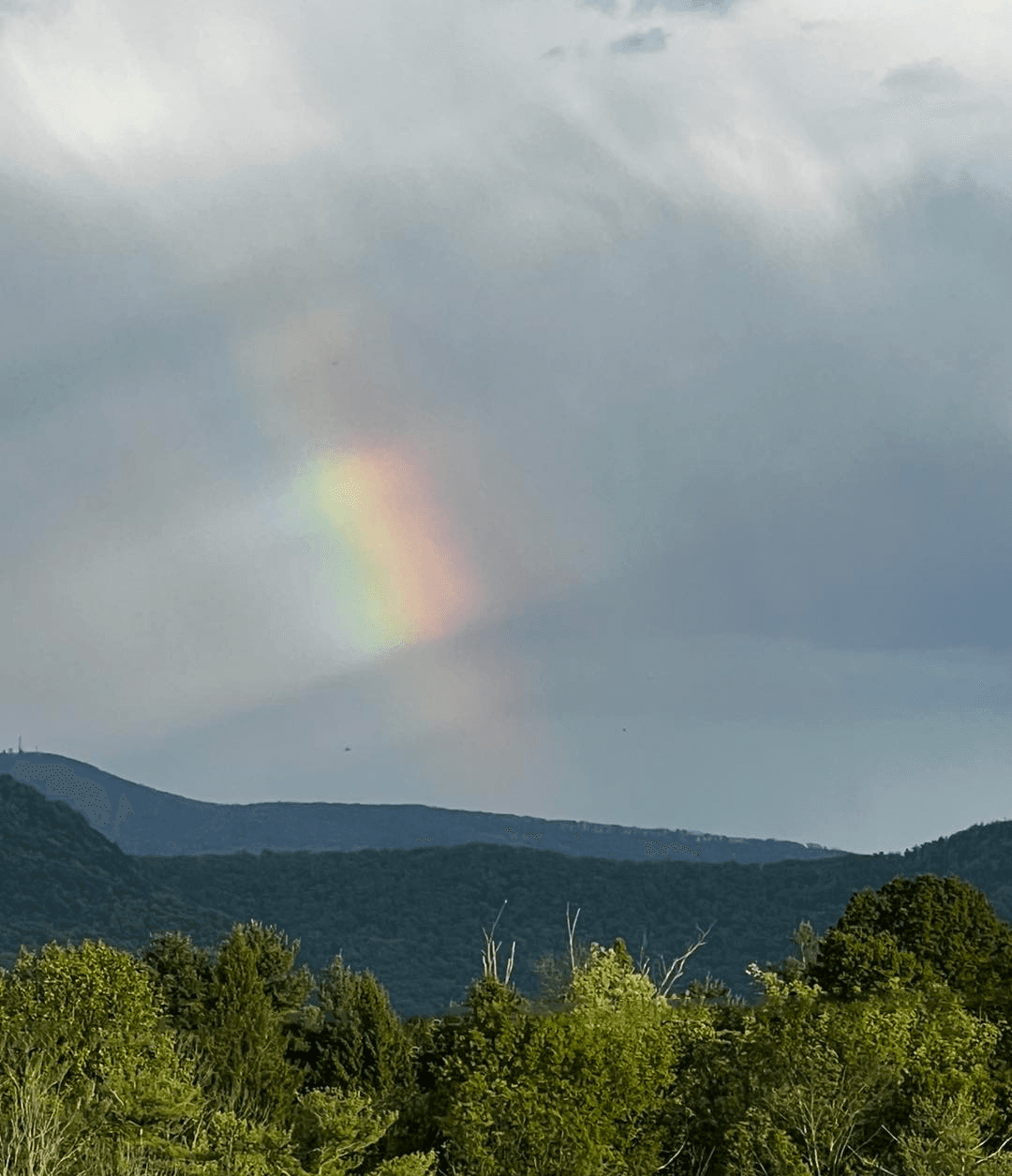 A faint rainbow arcs across a cloudy sky over green mountains.