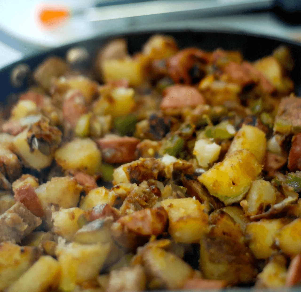 A close-up of sizzling diced potatoes, sausage, and green peppers in a frying pan.