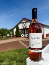 A bottle of rosé wine sits on a white post with a winery building in the background.
