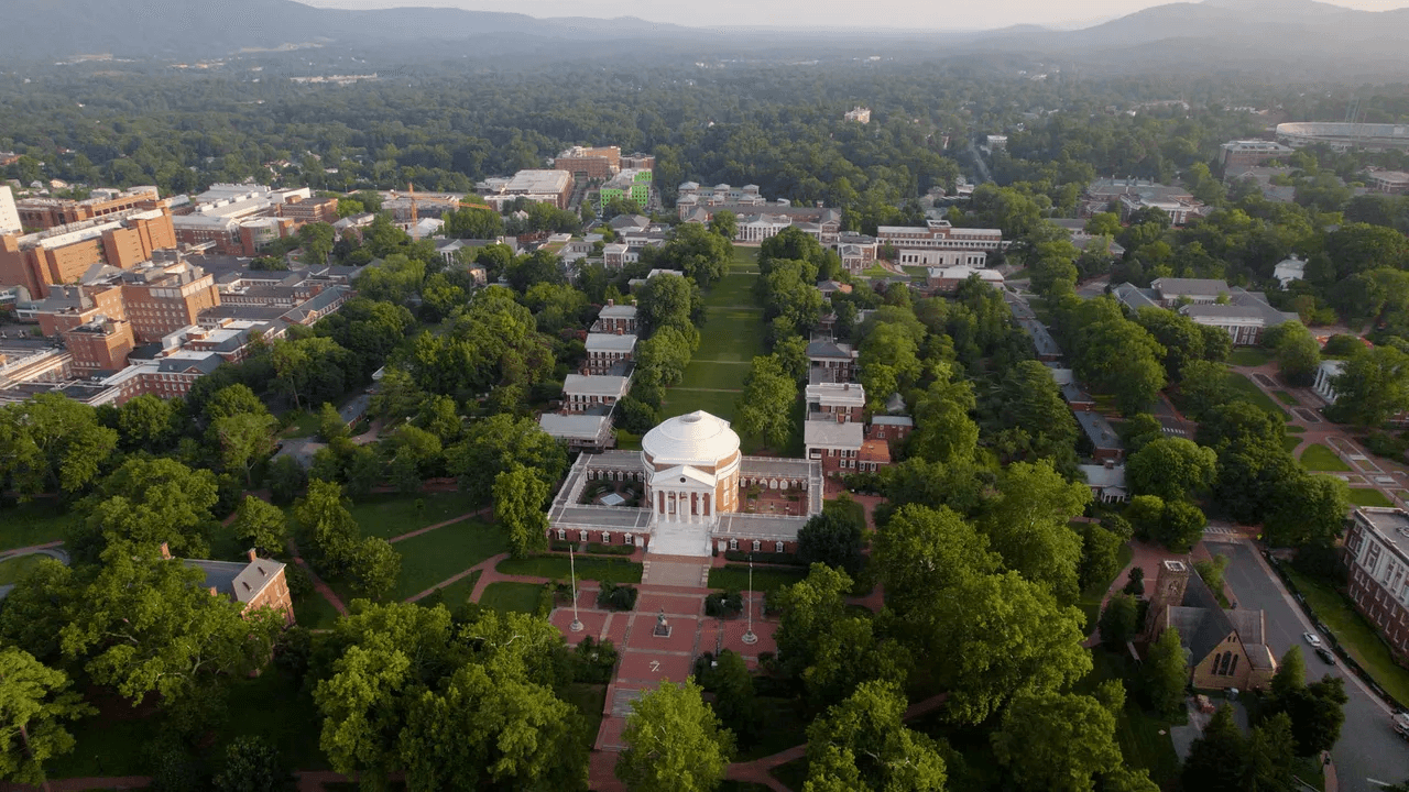 Aerial view of a university campus surrounded by lush greenery and mountains in the background.