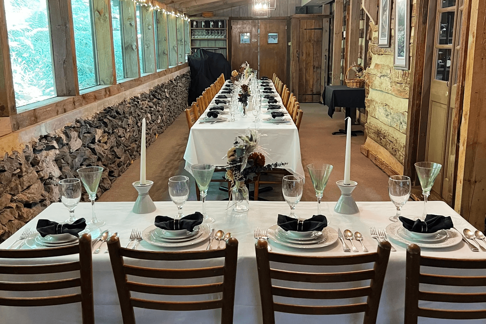 A beautifully set long dining table with elegant tableware and floral arrangements in a rustic wooden venue.