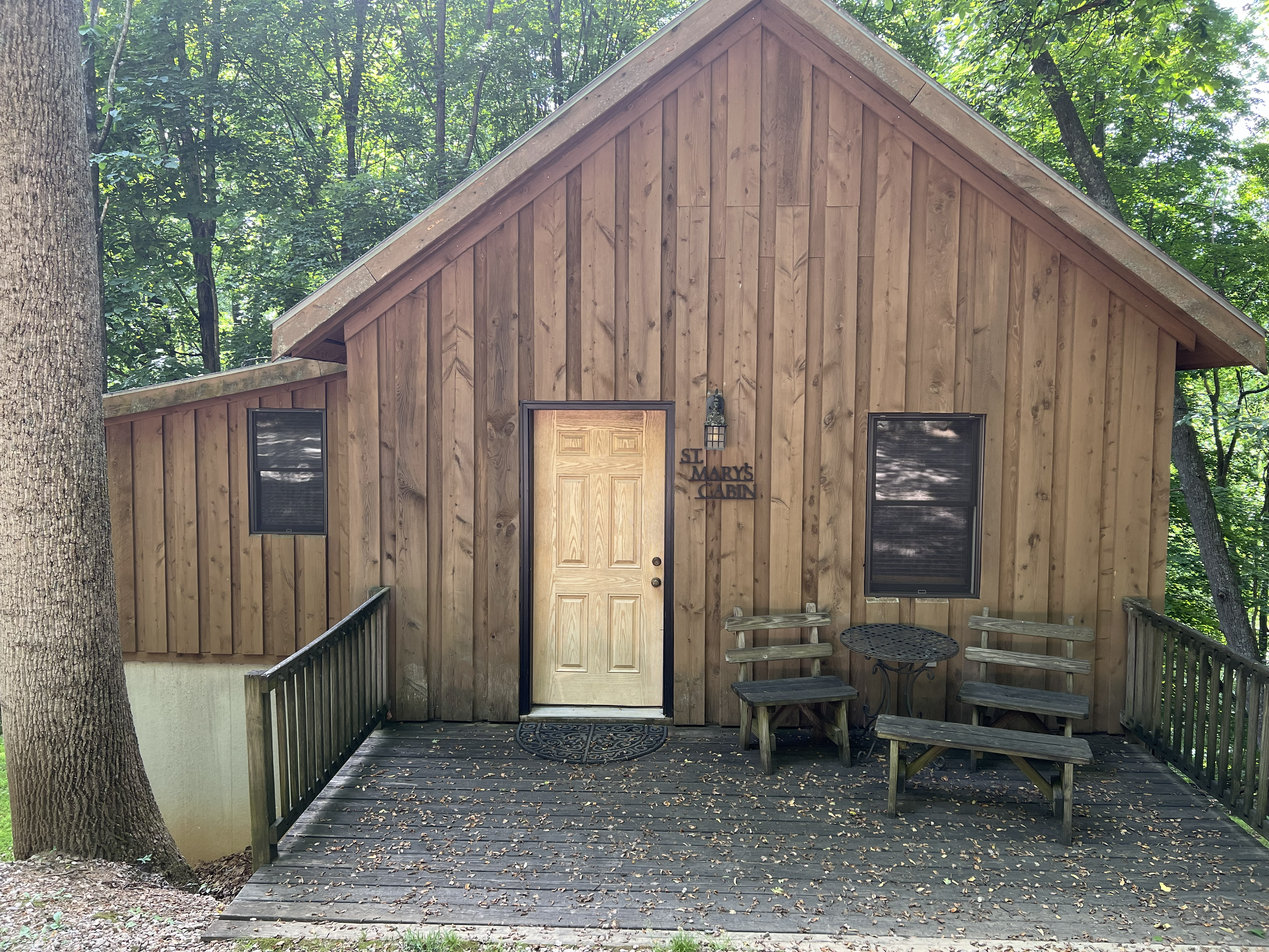 A rustic brown cabin with a white door and a small wooden bench, nestled amongst bare trees on a gravel path.