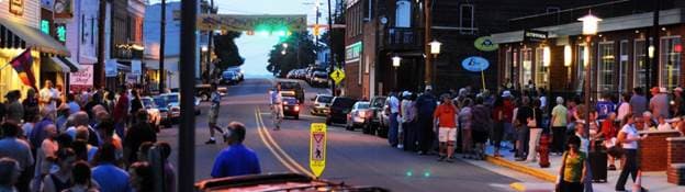 A bustling street scene at dusk with crowds gathered along the sidewalks.