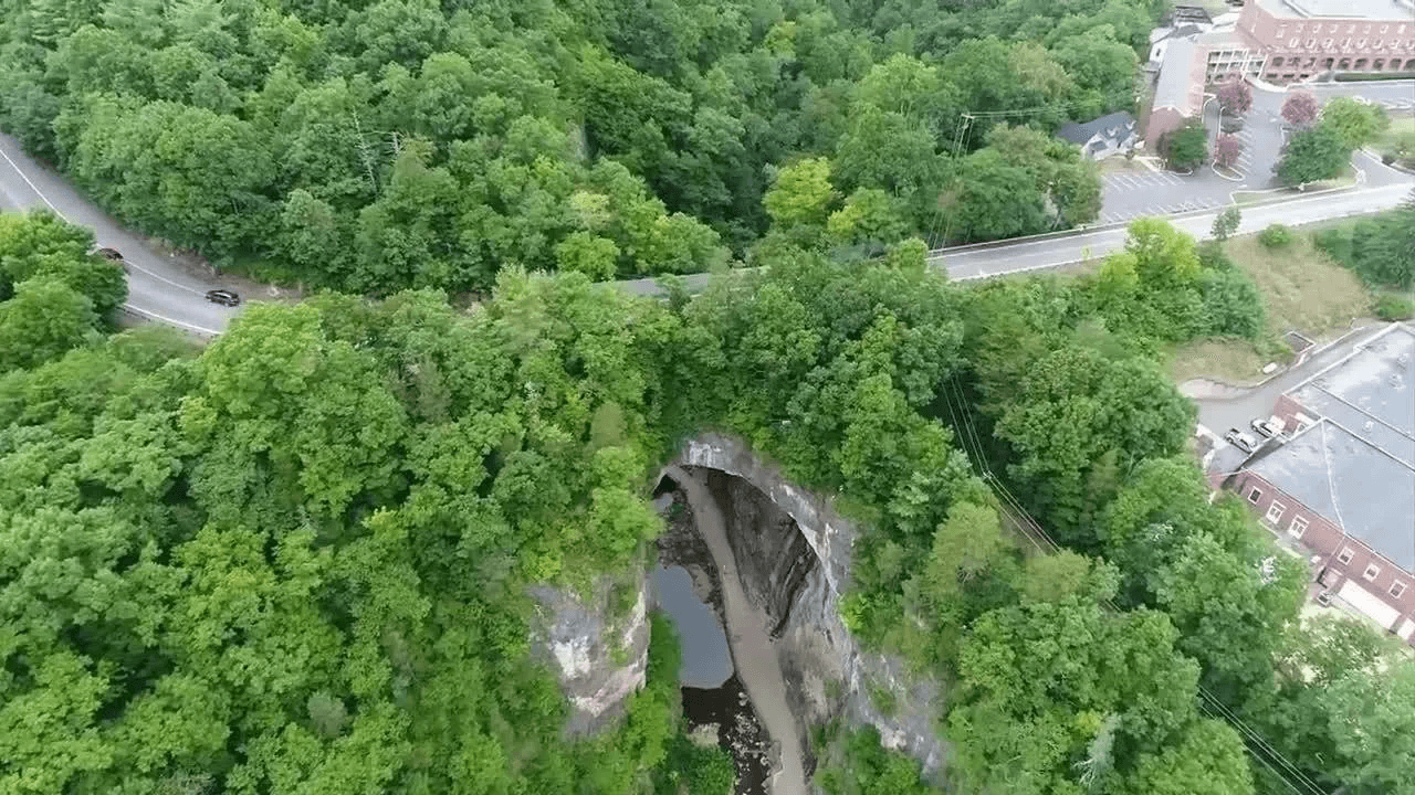 Aerial view of a lush green landscape featuring a rock formation and a winding road nearby.