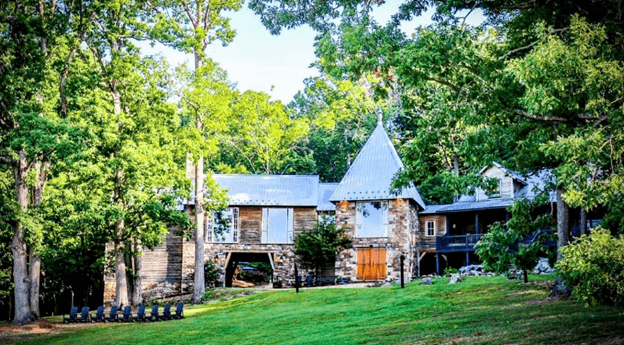 A charming stone house with a pointed roof surrounded by lush green trees.