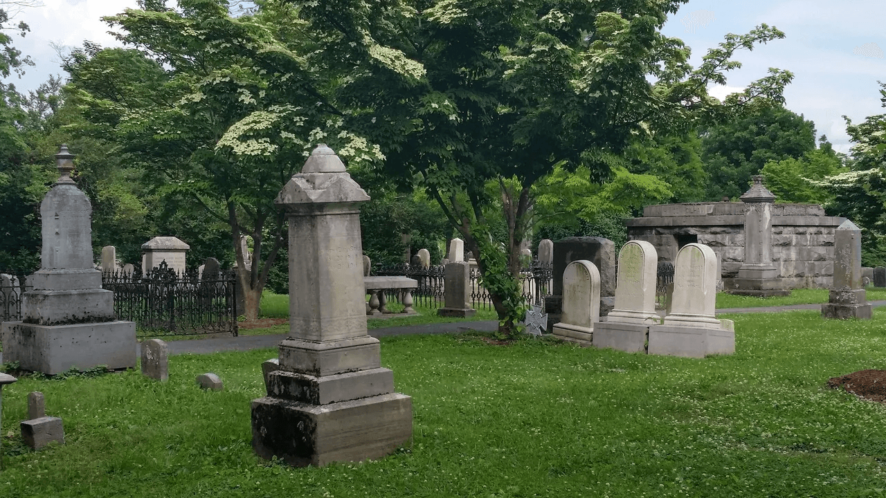 A peaceful cemetery with various gravestones set amidst green grass and trees.